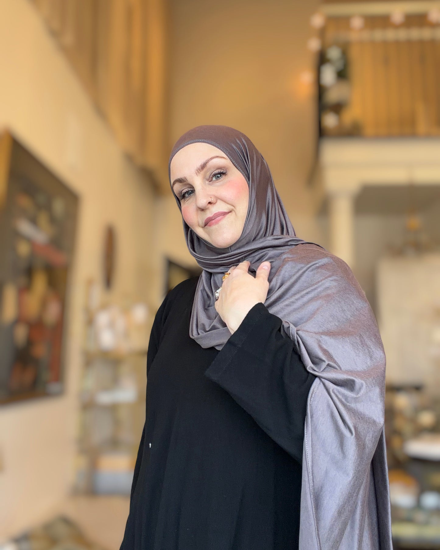 Woman wearing a gray hijab and black outfit indoors