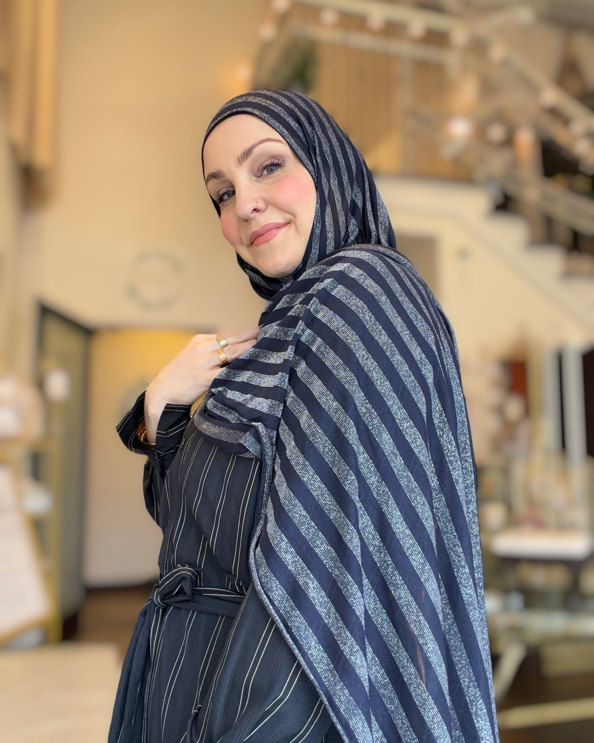 Woman wearing a striped headscarf and coat in an indoor setting